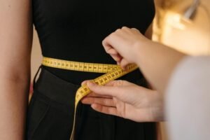 Why Professional Clothing Alterations Matter Close-up of tailor's hands measuring a person's waist with a yellow tape.